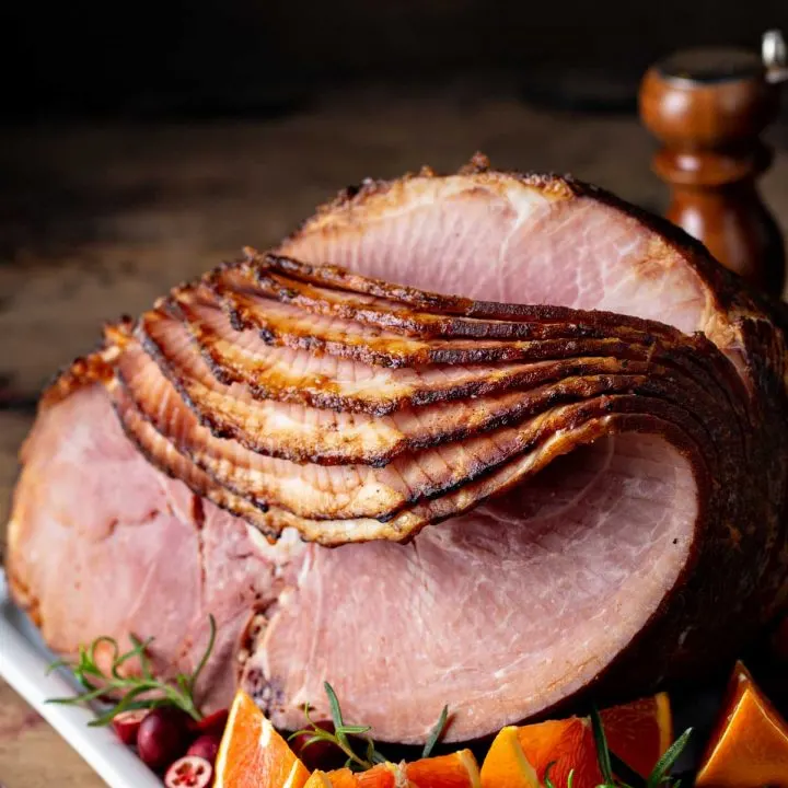 a spiral sliced ham on a white plate with fresh orange wedges on a wood table