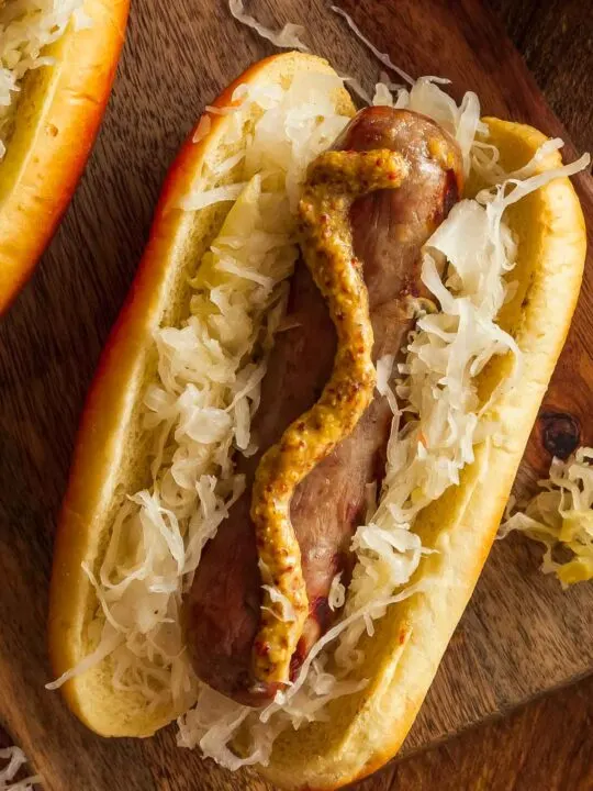 Brats Made In An Air Fryer on a Bun Topped With Mustard and Sauerkraut