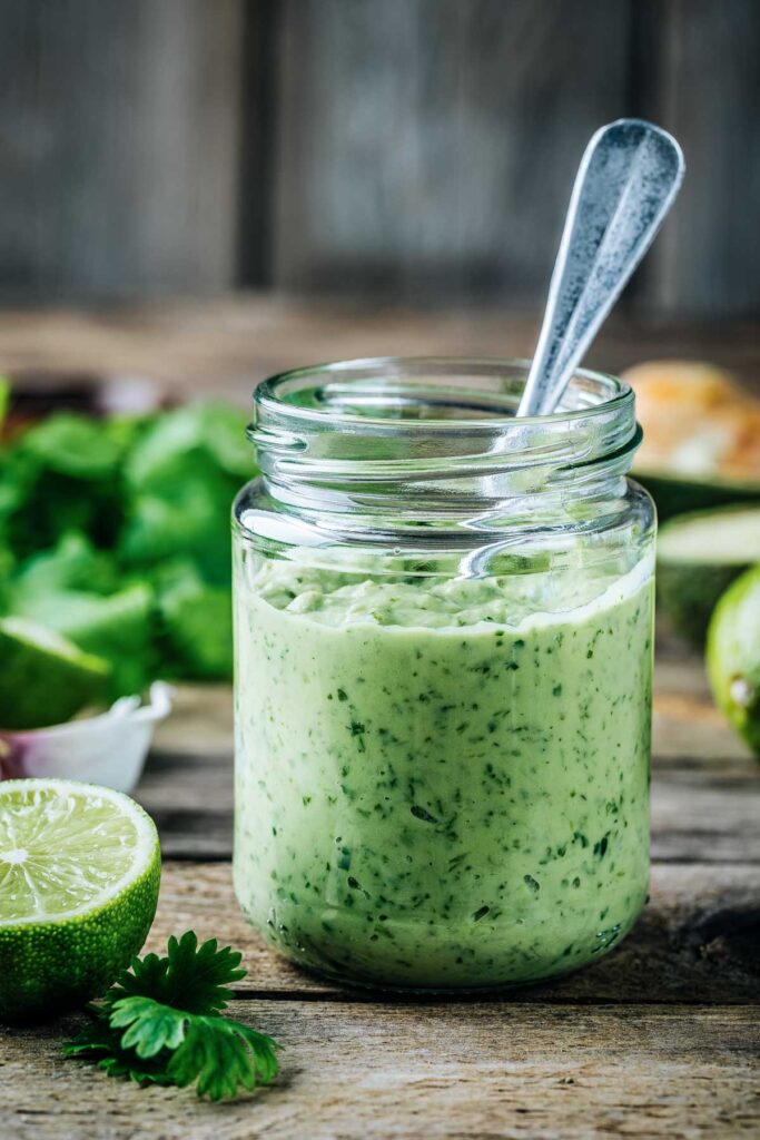 a jar of avocado lime ranch dressing with a spoon next to lime wedges and cilantro sprigs