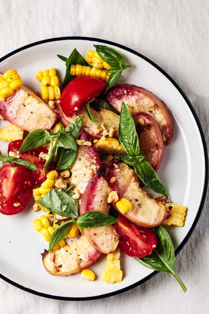 grilled peach salad on a white plate with corn and tomatoes