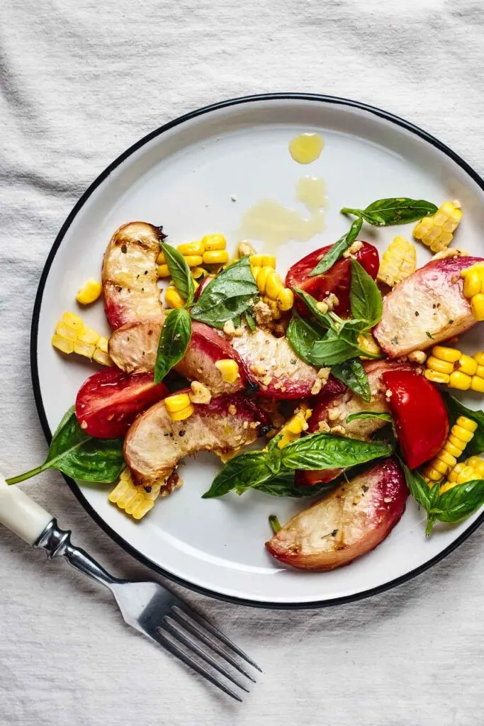grilled peach salad with basil vinaigrette on a white plate with corn and tomatoes