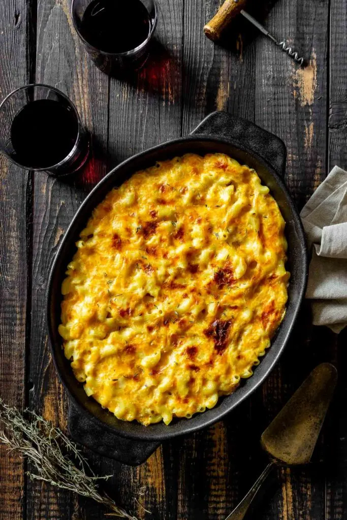 smoked mac and cheese in a cast iron pan on a dark wooden table next to two glasses of red wine