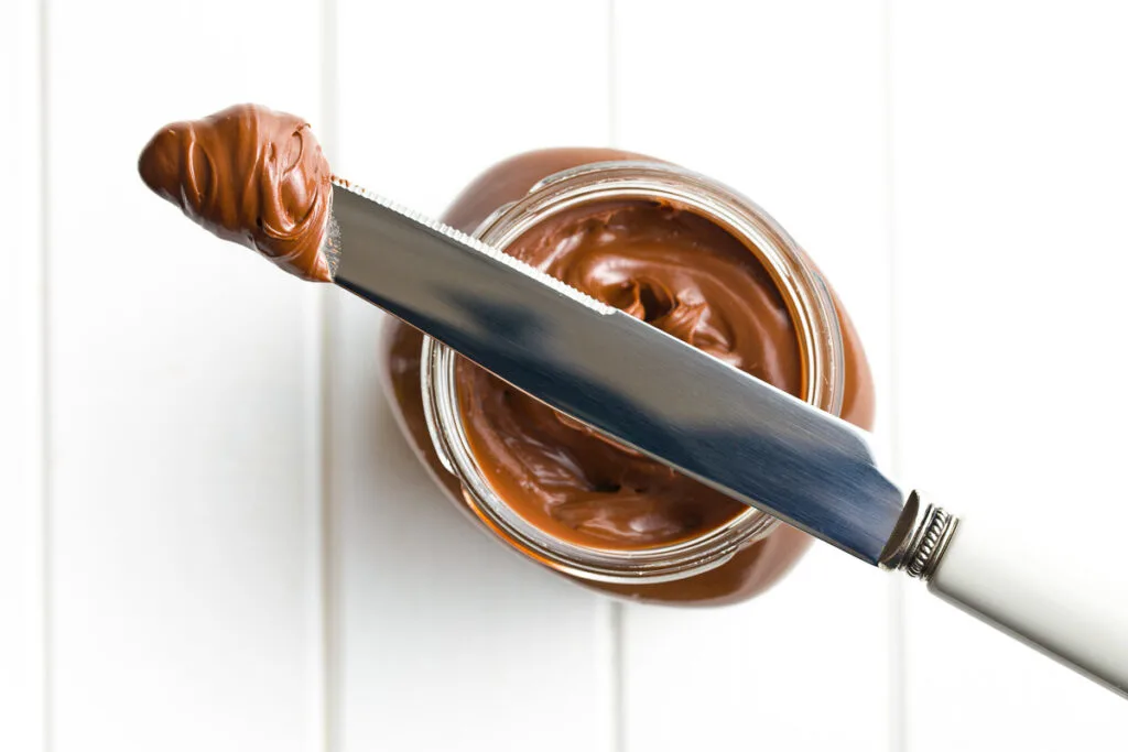 an overhead shot of a jar of nutella with a knife for pancake toppings