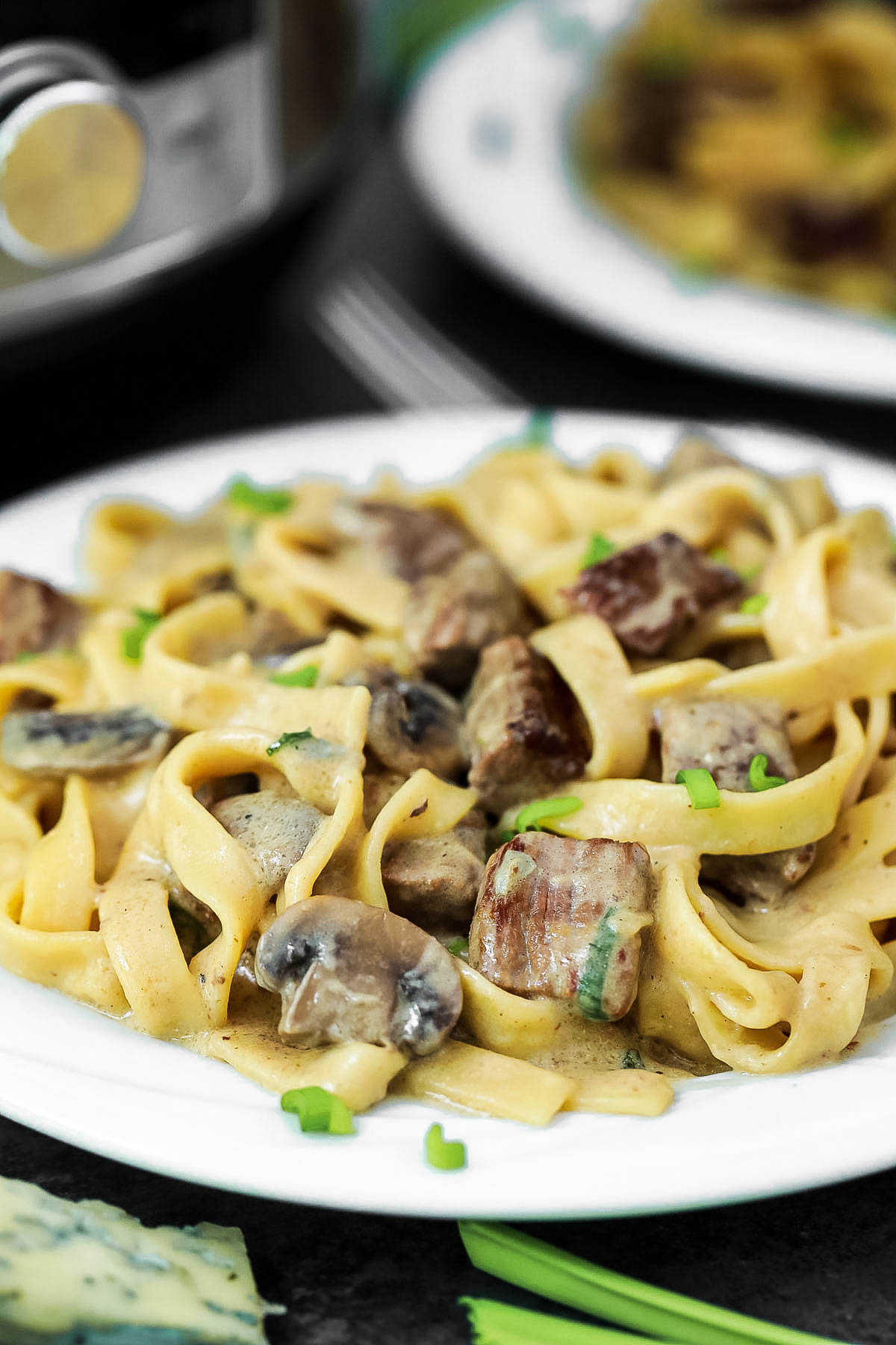 Instant Pot Beef Stroganoff with Blue Cheese and Chives on a white Plate, with another plate and an instant pot in the background