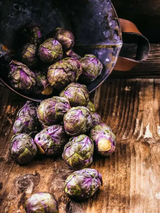 Purple Brussels Sprouts Spilling Out Onto A Wood Cutting Board