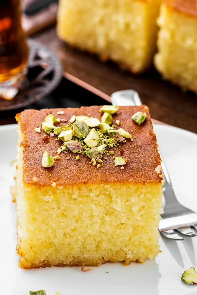 a closeup of a slice of revani turkish cake on a white plate garnished with pistachios