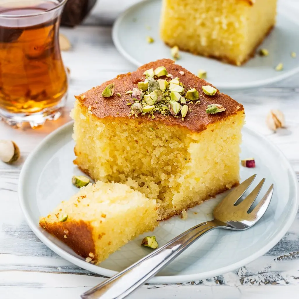 a slice of revani turkish cake on a white plate garnished with pistachios