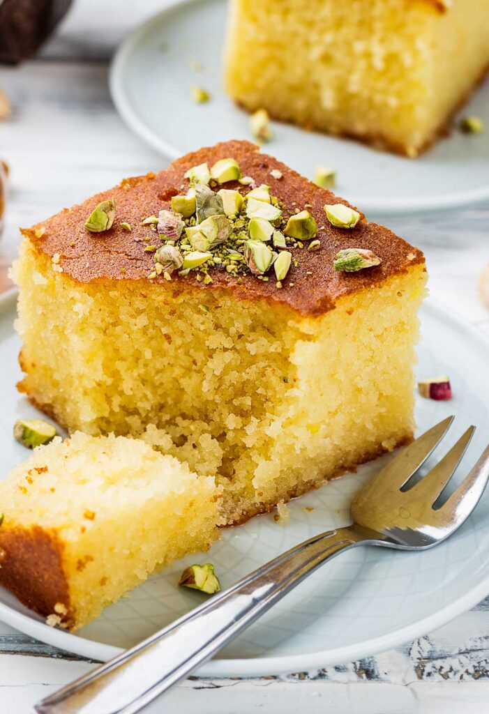 a closeup of a slice of revali turkish cake on a white plate garnished with pistachios