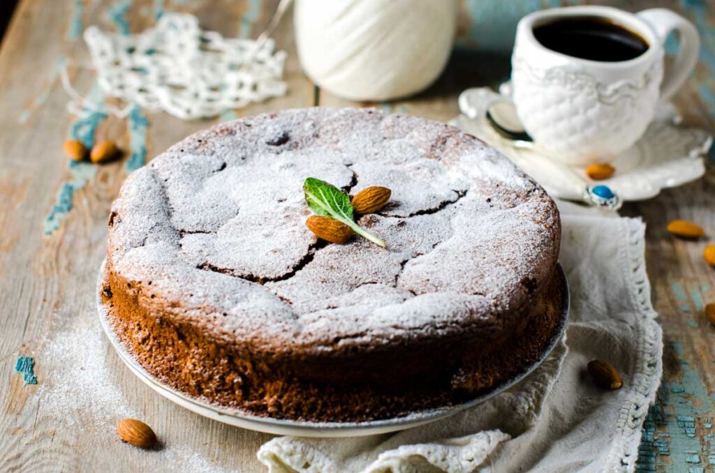 The Best Almond Flour Chocolate Cake – No Mixer Needed! an almond flour chocolate cake, dusted with powdered sugar and garnished with two fresh almonds