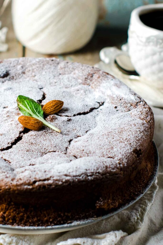 The Best Almond Flour Chocolate Cake – No Mixer Needed! a closeup of an almond flour chocolate cake, dusted with powdered sugar and garnished with two fresh almonds
