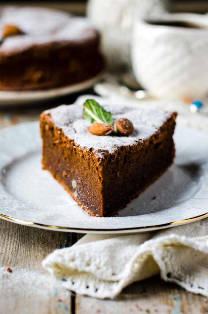 a slice of almond flour chocolate cake, dusted with powdered sugar and garnished with two fresh almonds