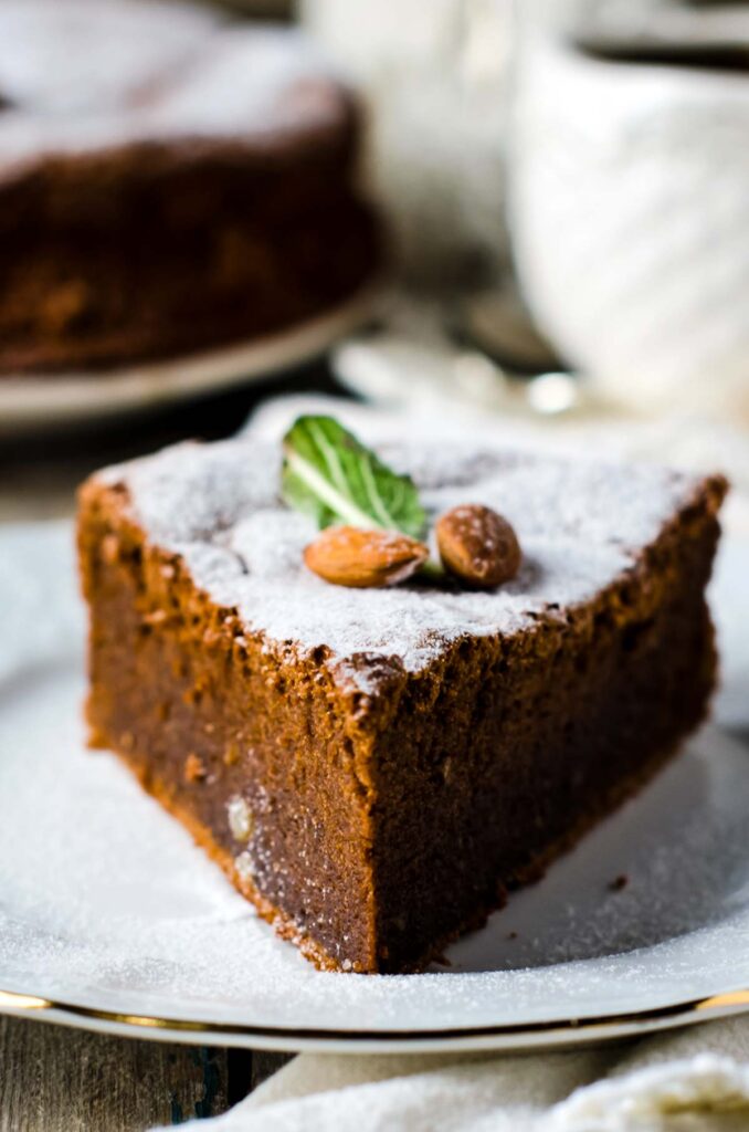 The Best Almond Flour Chocolate Cake – No Mixer Needed! a closeup of a slice of almond flour chocolate cake, dusted with powdered sugar and garnished with two fresh almonds