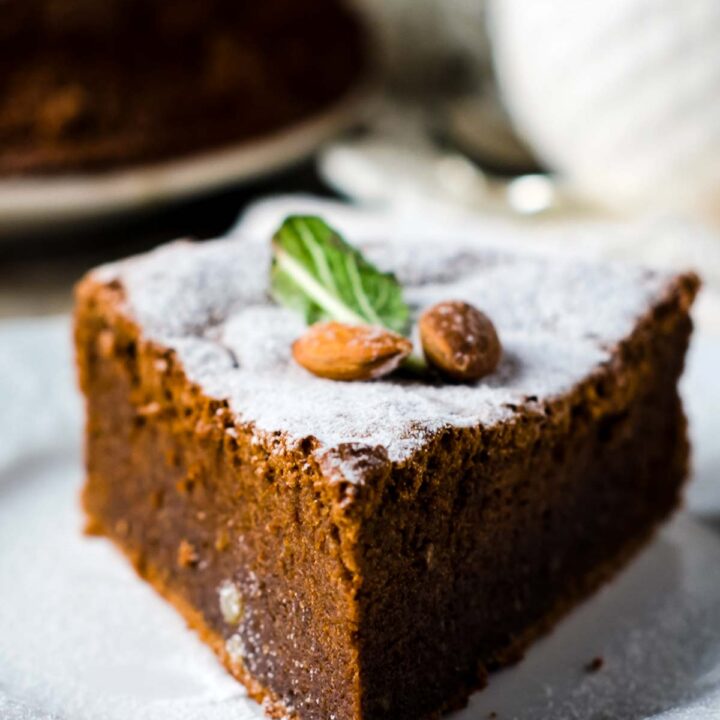 a closeup of a slice of almond flour chocolate cake, dusted with powdered sugar and garnished with two fresh almonds