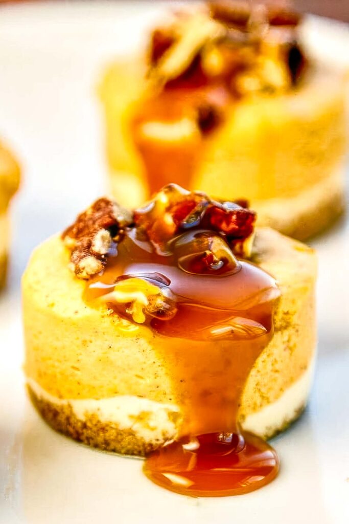 Mini pumpkin cheesecakes on a plate with pecan topping and golden caramel drizzle