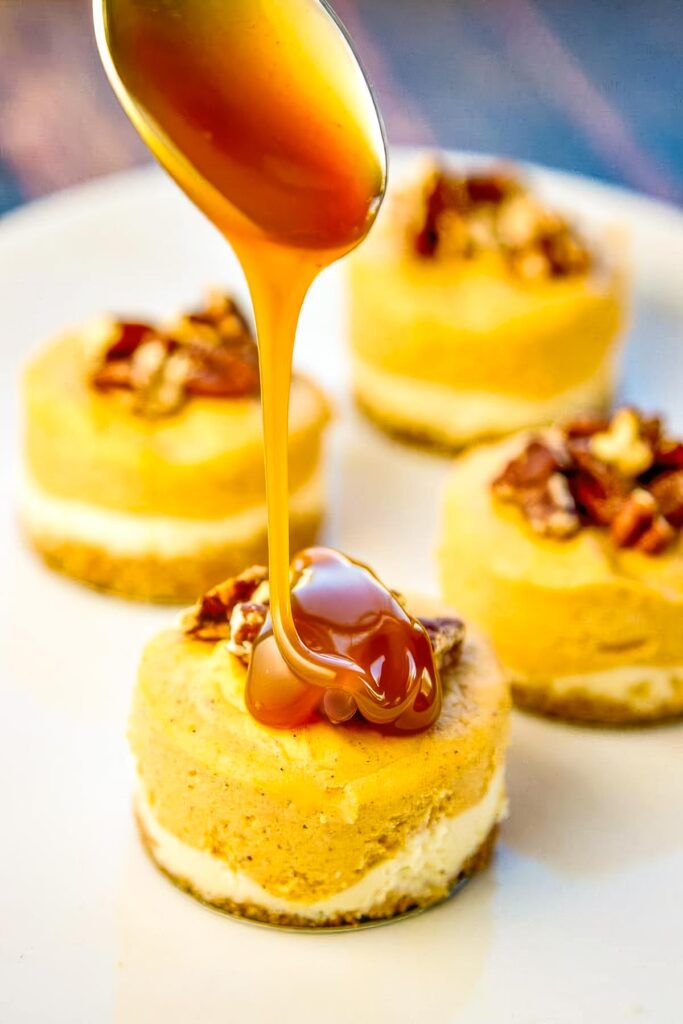 Spoon pouring caramel onto pumpkin cheesecake with pecans on a white plate