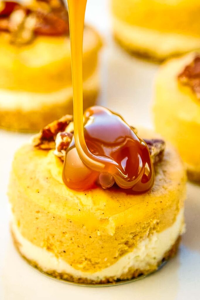 Close-up of caramel being poured over a mini pumpkin cheesecake topped with pecans