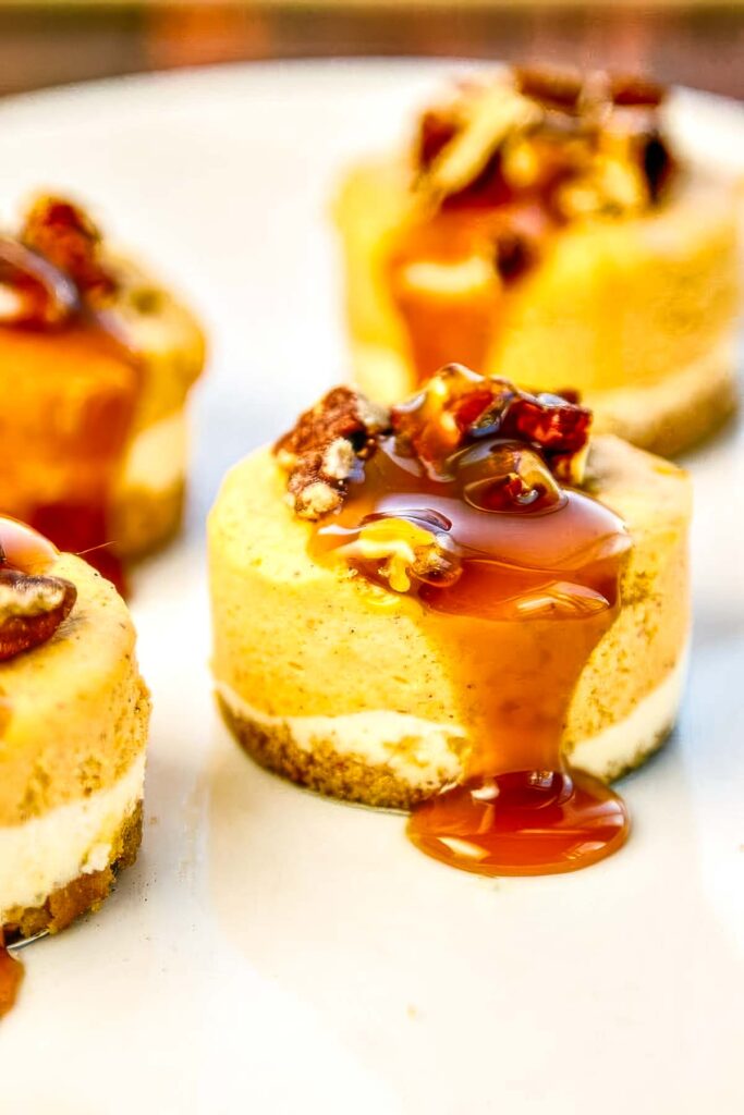 Pumpkin cheesecake topped with chopped pecans and a thick drizzle of caramel sauce