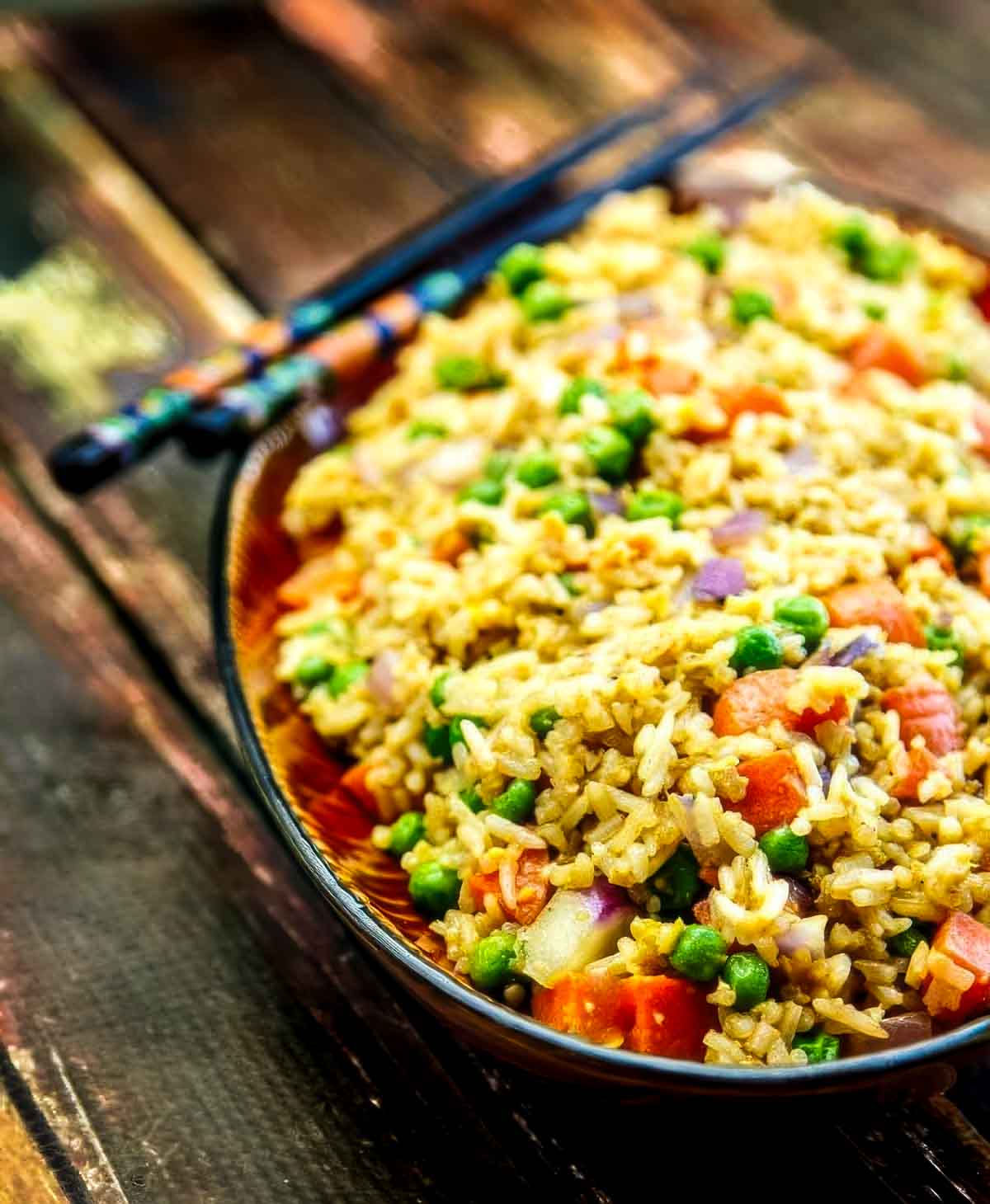 Easy Fried Rice – The Ultimate “Use What You Have” Dinner a platter of easy fried rice on a wooden table with two chopsticks resting on the side of the dish