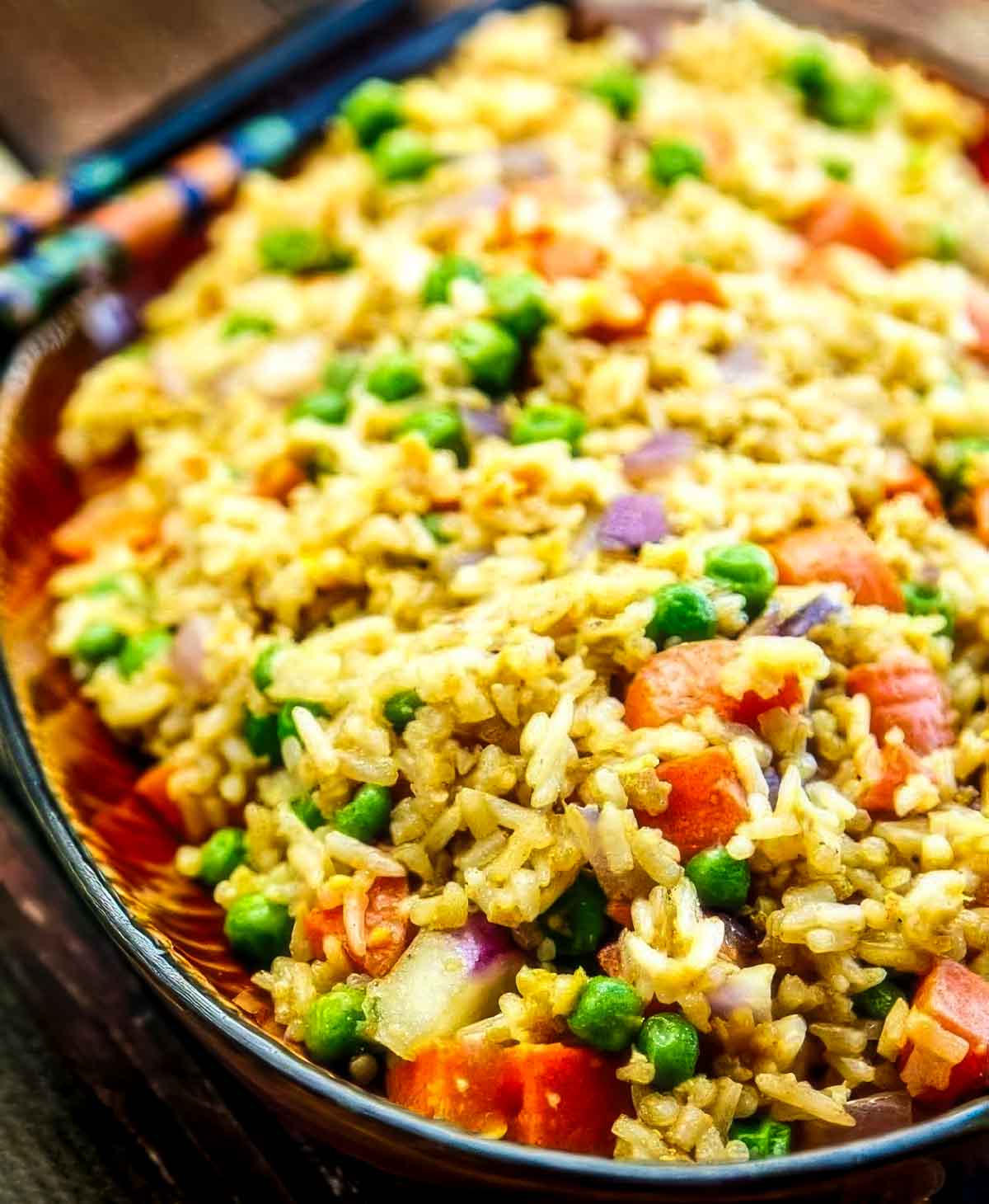a closeup of a platter of easy fried rice on a wooden table with two chopsticks resting on the side of the dish