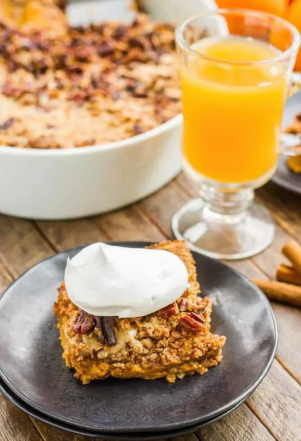 a slice of pumpkin pie cake on a black plate topped with fresh whipped cream, next to a glass of apple cider