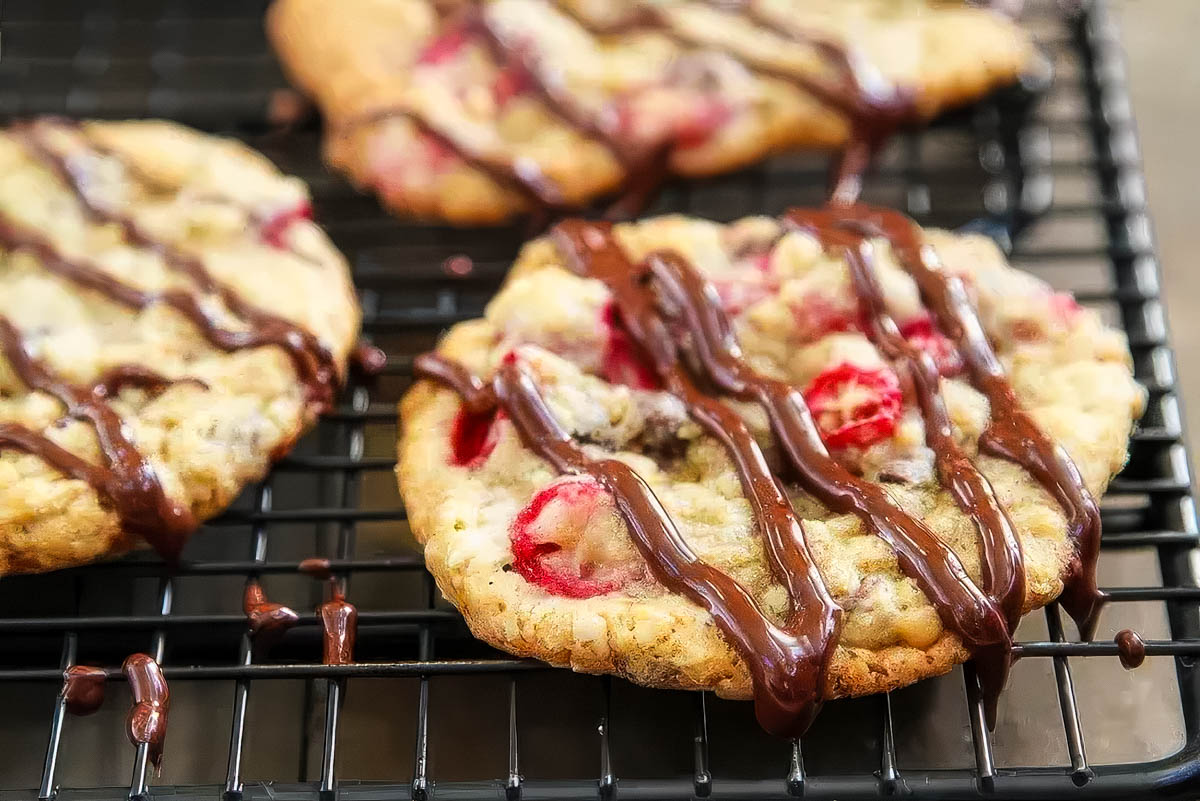 Cranberry Oatmeal Chocolate Chip Cookies a closeup of cranberry oatmeal chocolate chip cookies that have just been drizzled with melted chocolate are cooling on a wire rack