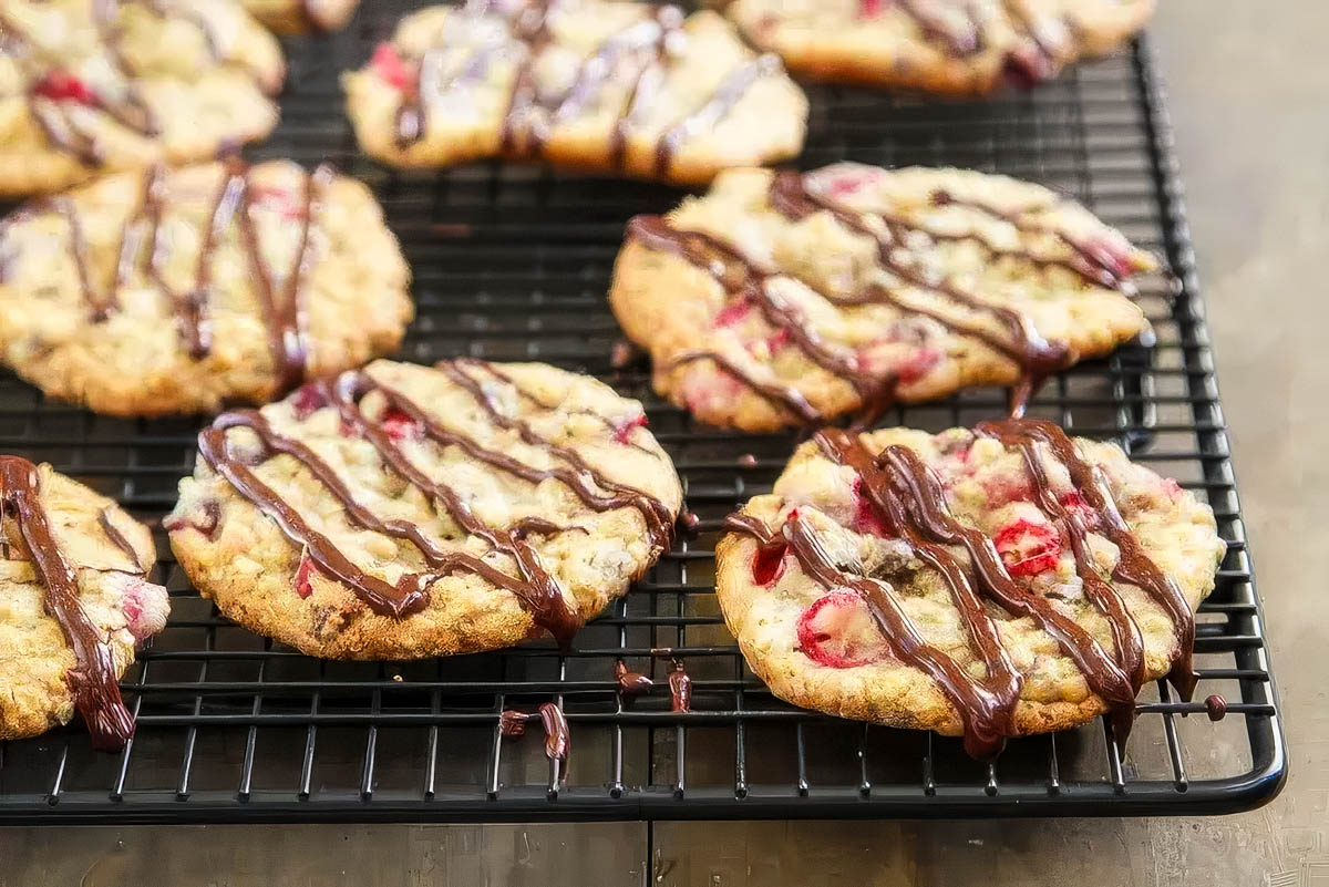 Cranberry Oatmeal Chocolate Chip Cookies cranberry oatmeal chocolate chip cookies drizzled with melted chocolate are cooling on a wire rack