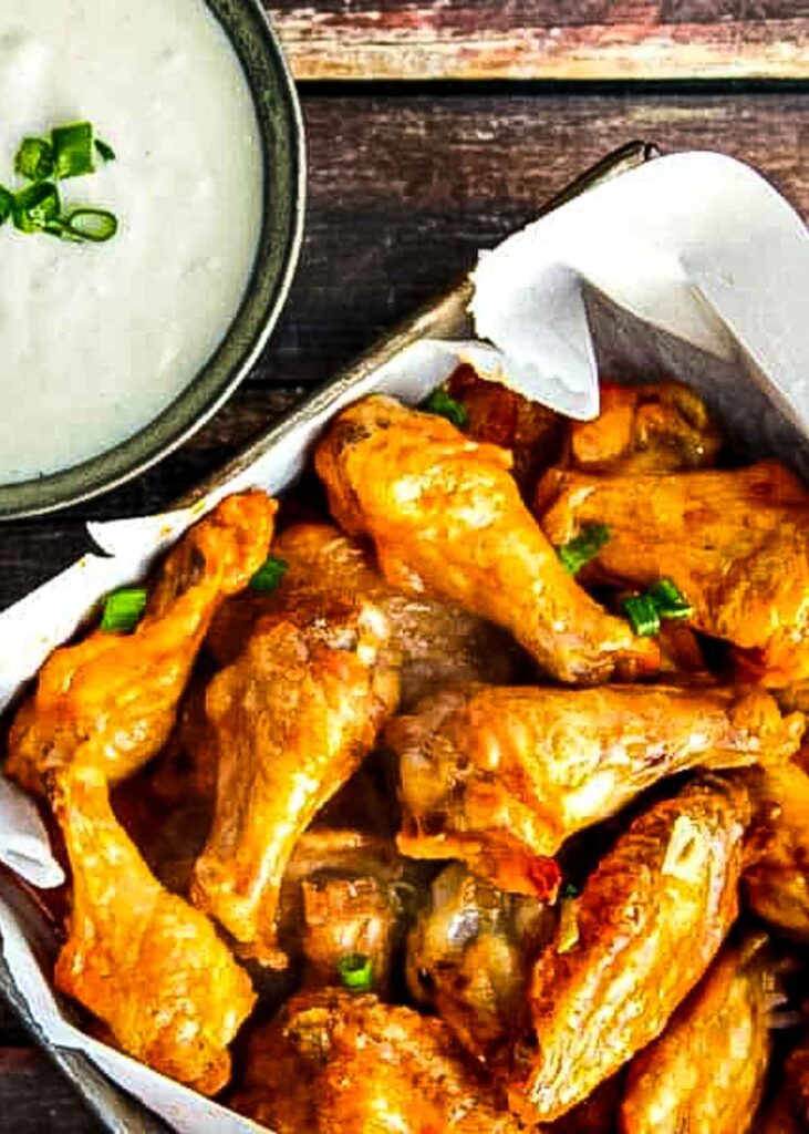spicy baked chicken wings are in a vintage metal dish lined with parchment paper next to a small dish of blue cheese dressing