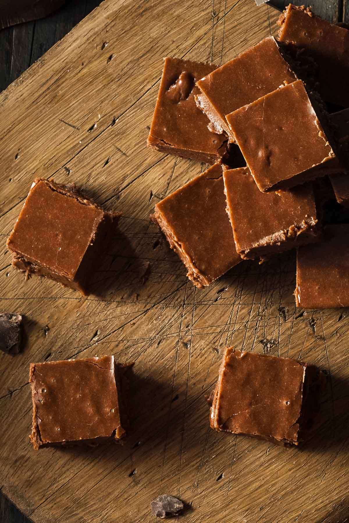 a closeup of an overhead shot of condensed milk fudge pieces on a wood cutting board