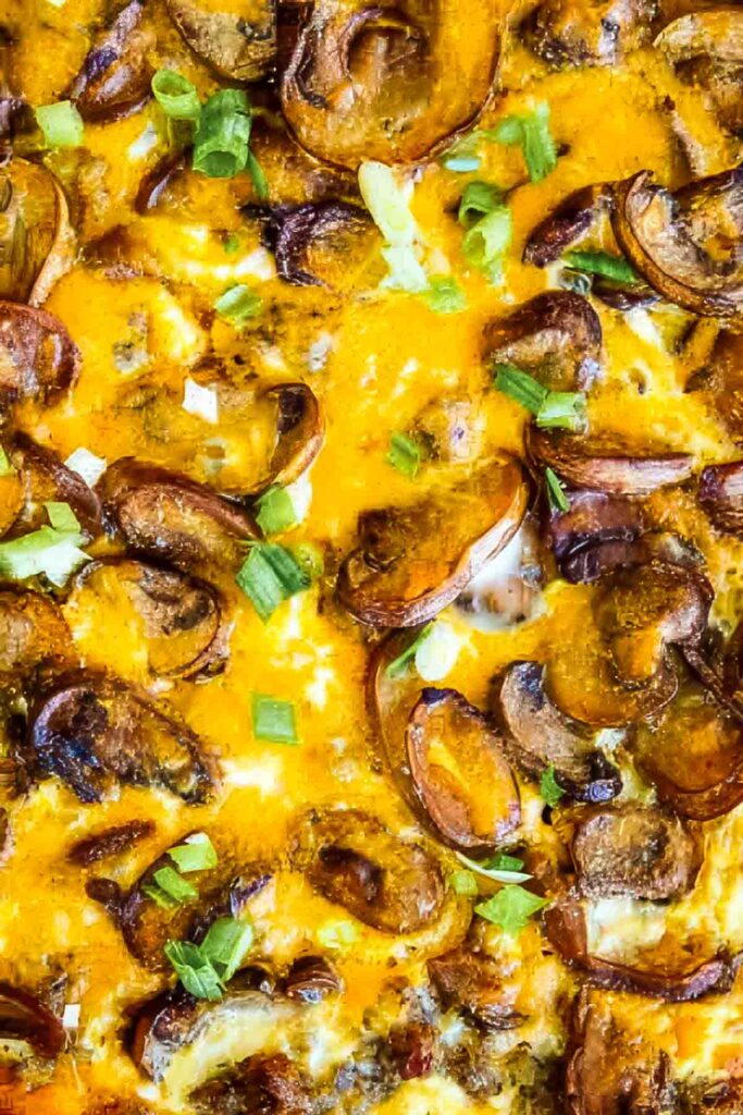 an extreme close-up view of a hash brown breakfast casserole and mushrooms and garnished with chopped green onions