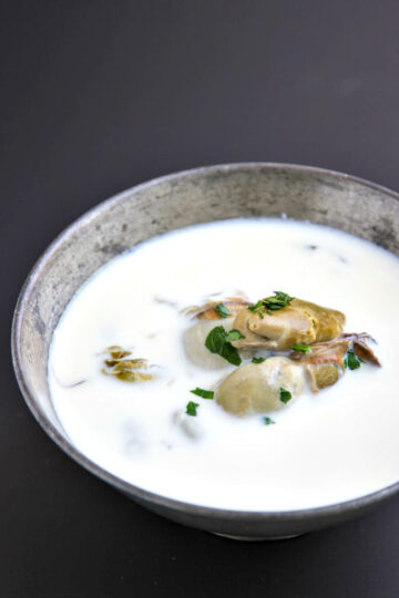 oyster stew with canned oysters in a vintage silver bowl on a black background