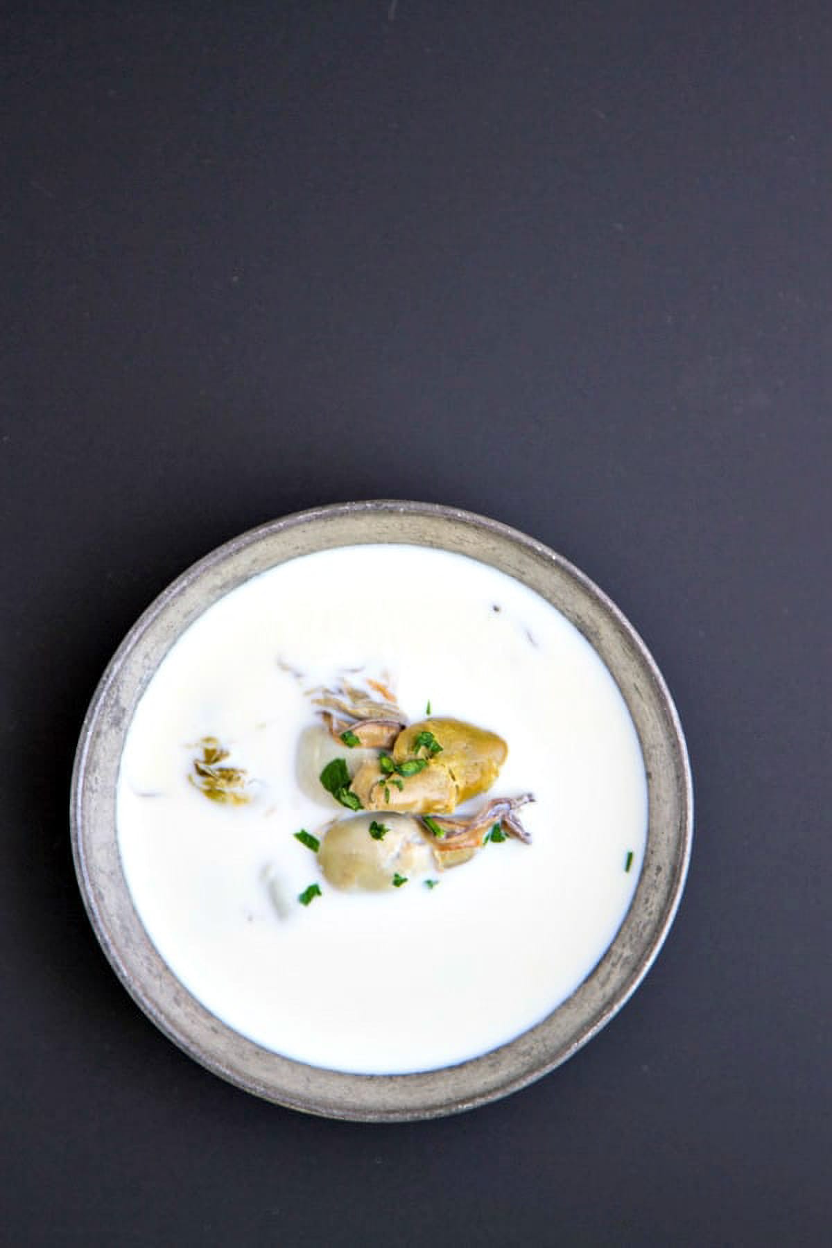 an overhead shot of oyster stew with canned oysters in a vintage silver bowl on a black background
