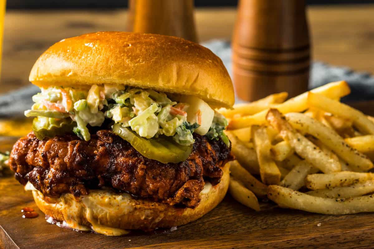 Nashville Hot Chicken Sandwich You Can Easily Make at Home a nashville hot chicken sandwich on a cutting board with french fries