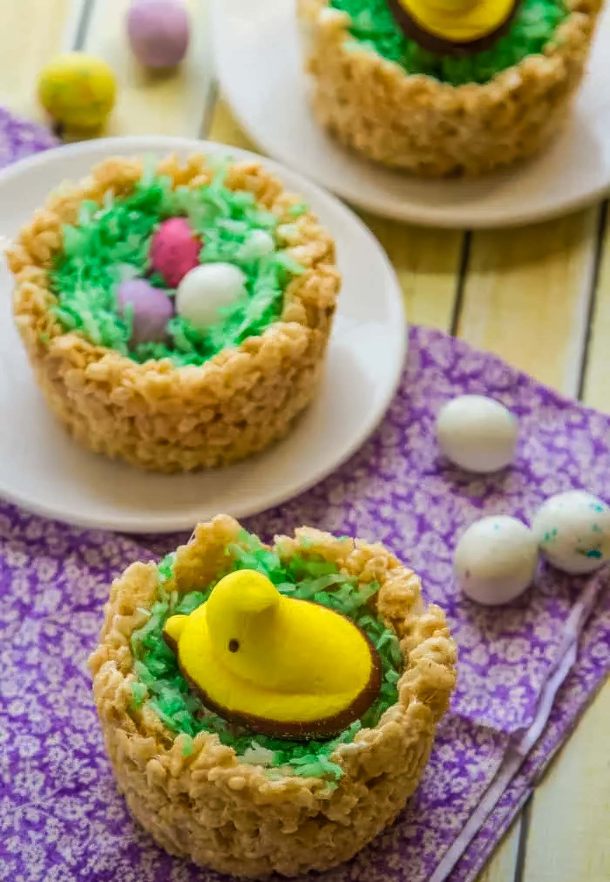two easter peeps nests (cupcakes), filled with green coconut flakes, one topped with a yellow chick peep and the other with small chocolate candy eggs