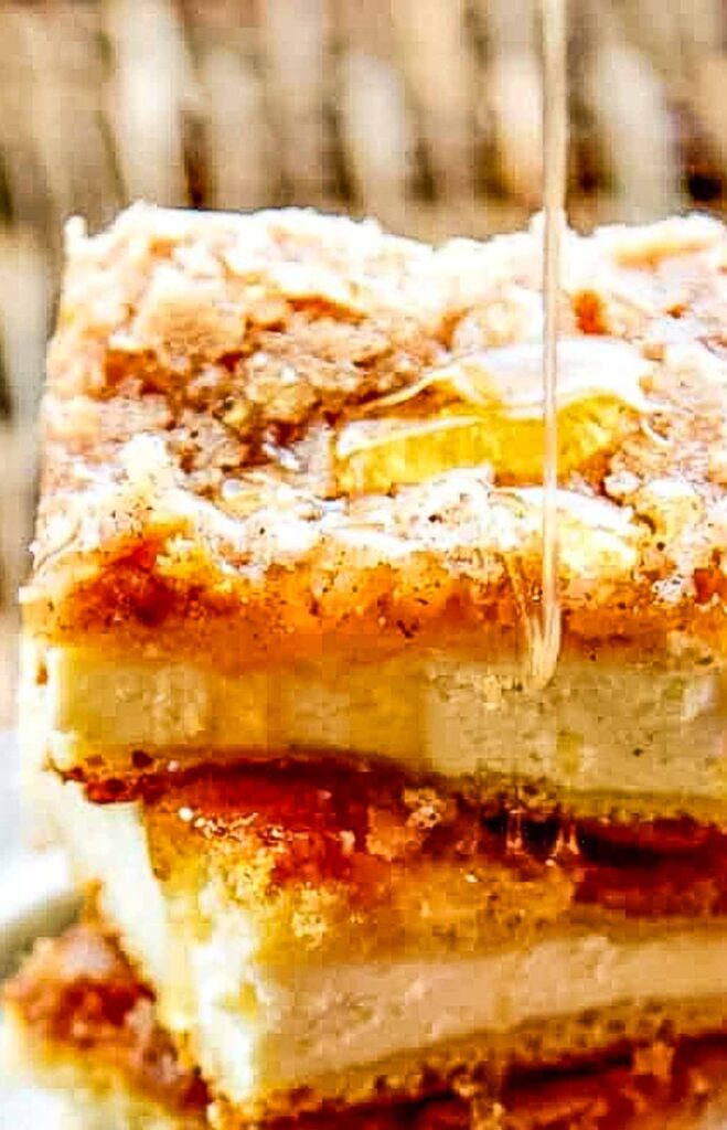 Side view of cinnamon sugar sopapilla cheesecake bars with honey being drizzled on top