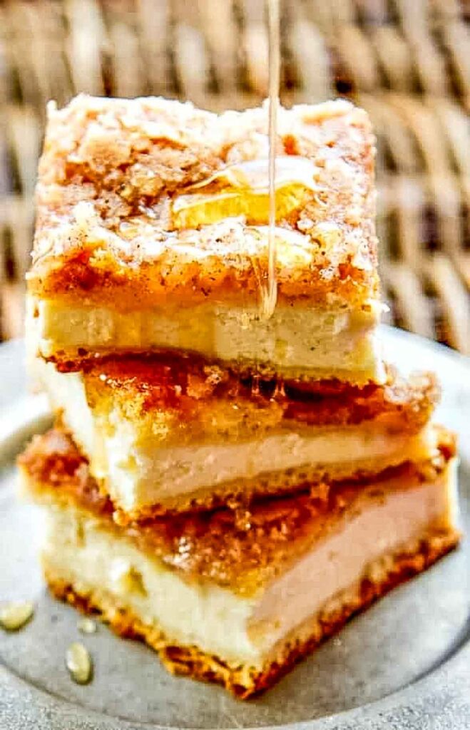 Three-layered sopapilla cheesecake bars stacked on a plate with honey drizzle mid-pour