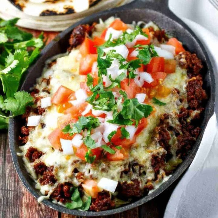 a cast iron skillet filled with choriqueso made with chorizo and cheese then topped with diced tomato, white onion, and cilantro