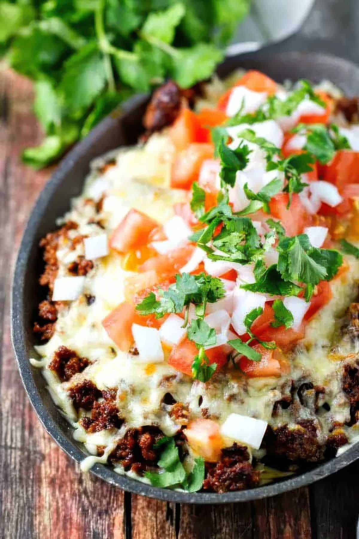 a closeup of a cast iron skillet filled with choriqueso made with chorizo and cheese then topped with diced tomato, white onion, and cilantro, next to a stack of charred flour tortillas