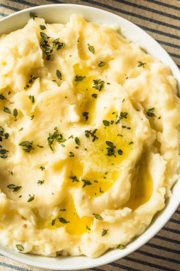 a white bowl filled with easy mashed potatoes and garnished with fresh thyme leaves