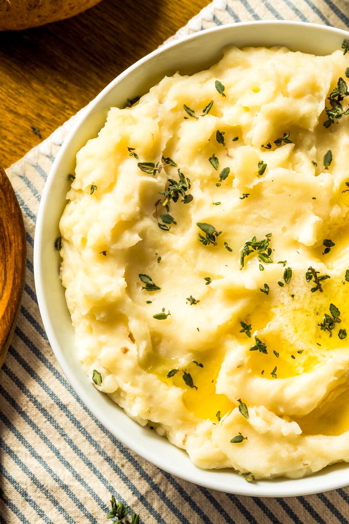 The Secret to Truly Easy Mashed Potatoes a white bowl filled with easy mashed potatoes and garnished with fresh thyme leaves