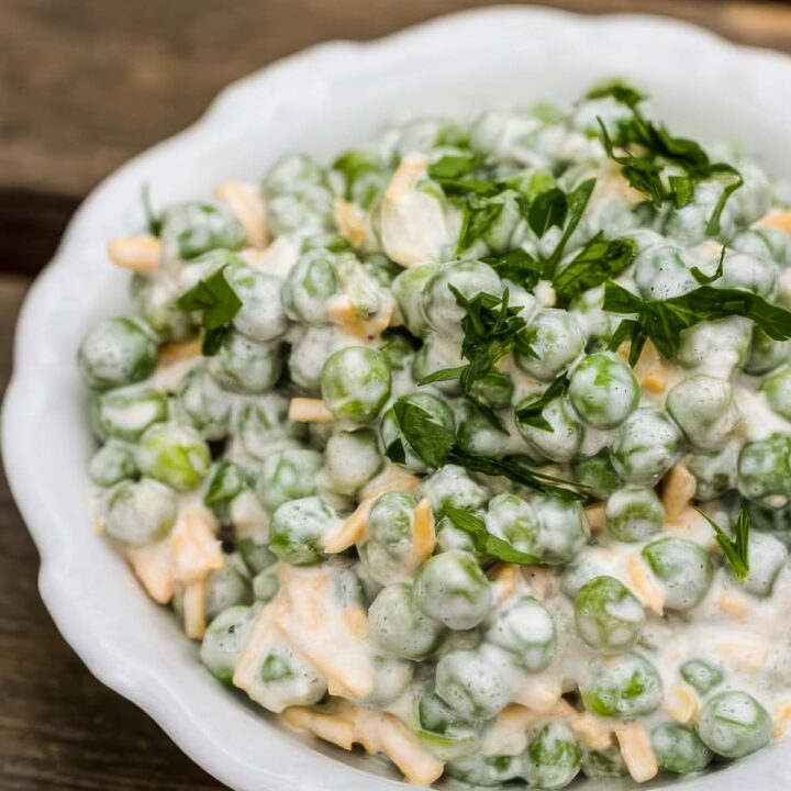 a white dish with scalloped edges, filled with an easy pea salad that's topped with chopped parsley on a wooden table