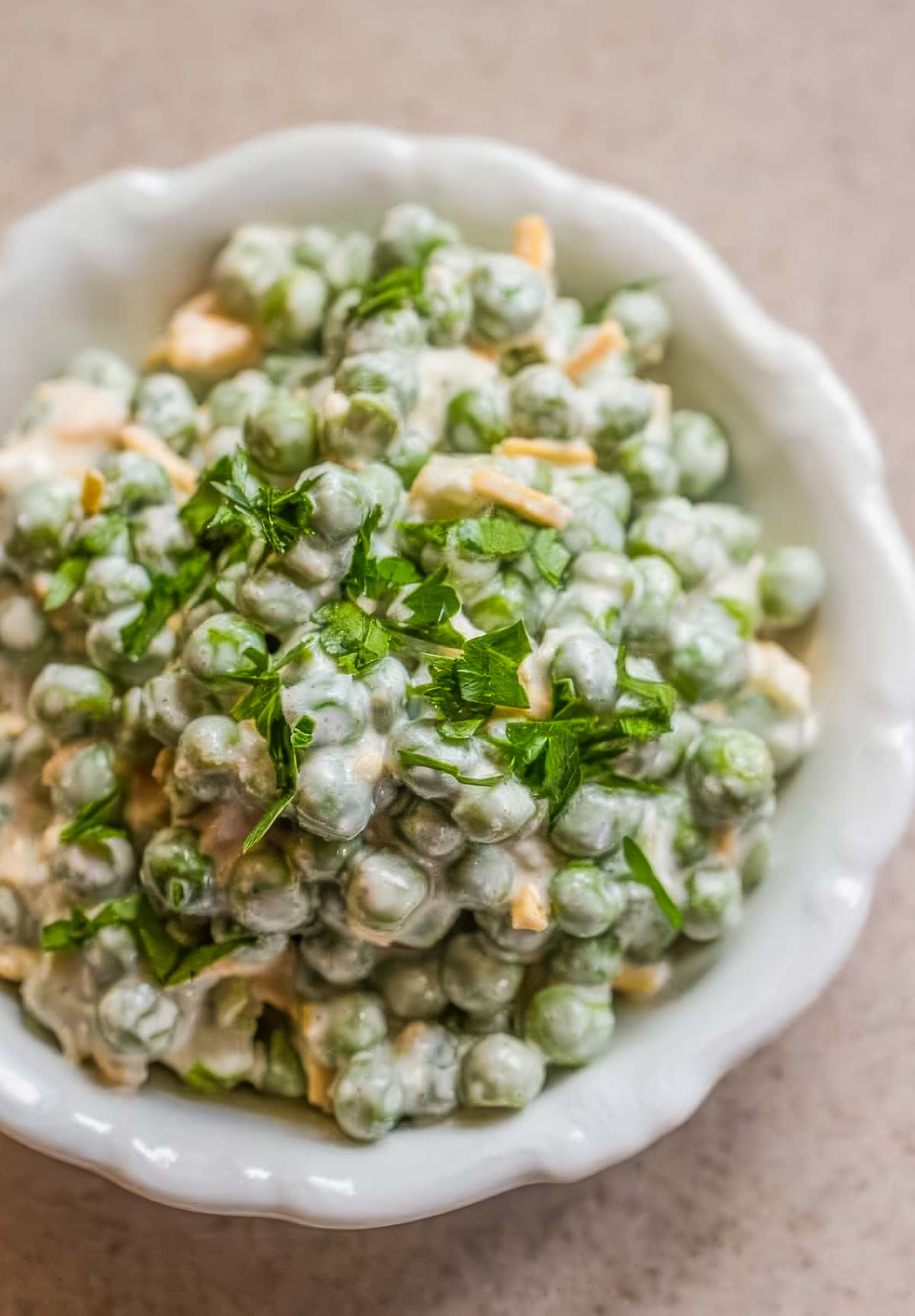 a white dish with scalloped edges, filled with an easy pea salad that's topped with chopped parsley