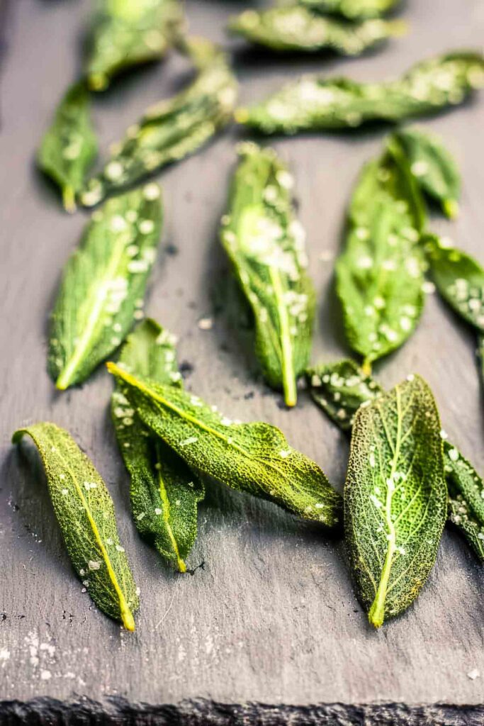 Fried sage leaves spread across a slate serving tray with a rustic wood background.