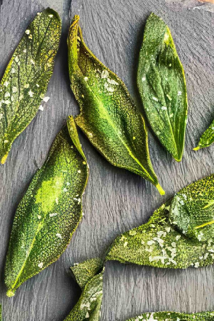 Close-up view of crispy fried sage leaves with visible salt crystals and detailed leaf texture.
