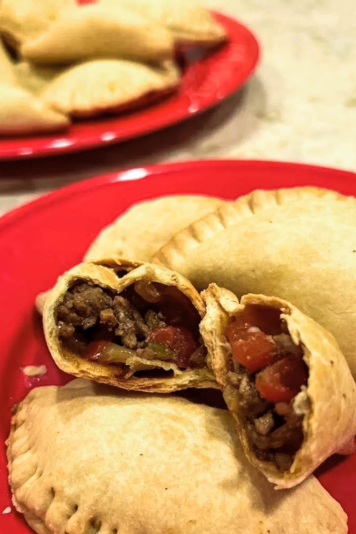 hot pastechi just out of the oven on a red plate, with one cut in half with the beef filling exposed