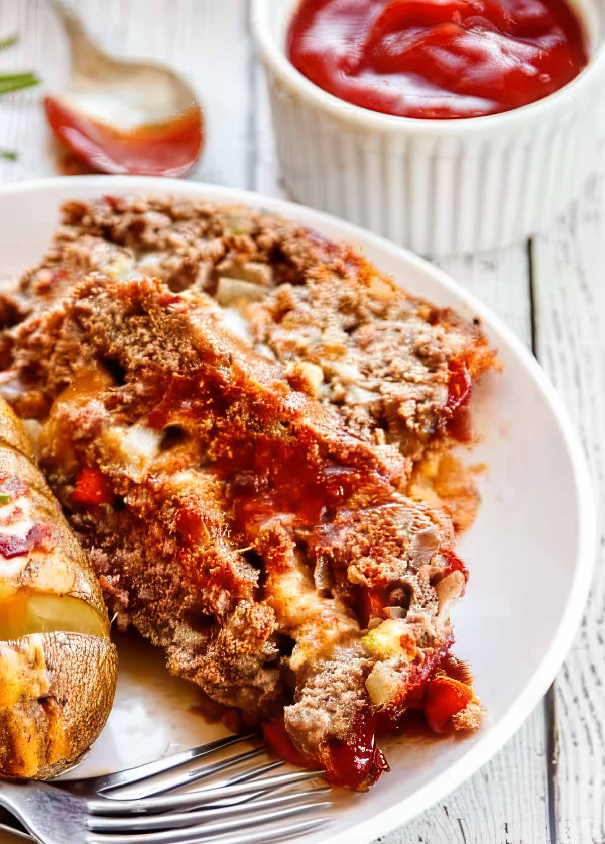 two slices of brown sugar meatloaf on a white plate with a small dish of the meatloaf glaze on the table