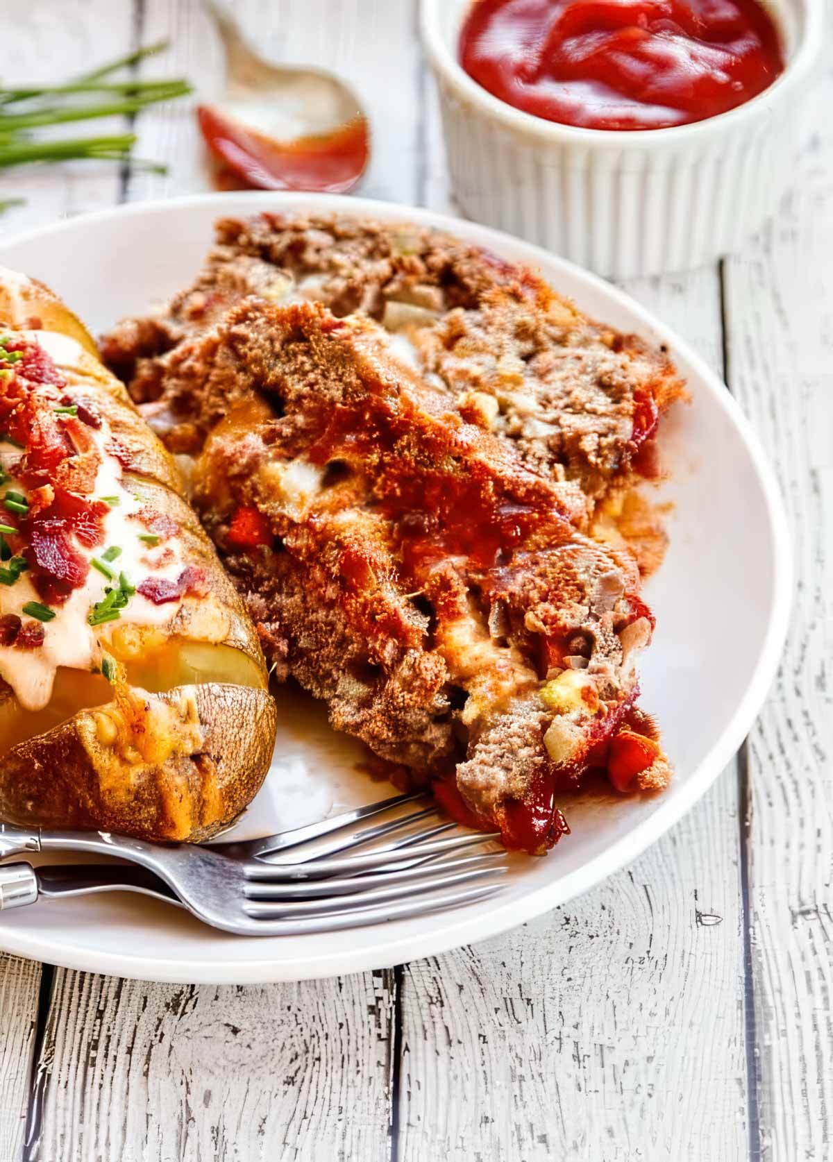Brown Sugar Meatloaf with Chipotle Gouda two slices of brown sugar meatloaf on a white plate with a loaded hasselback potato