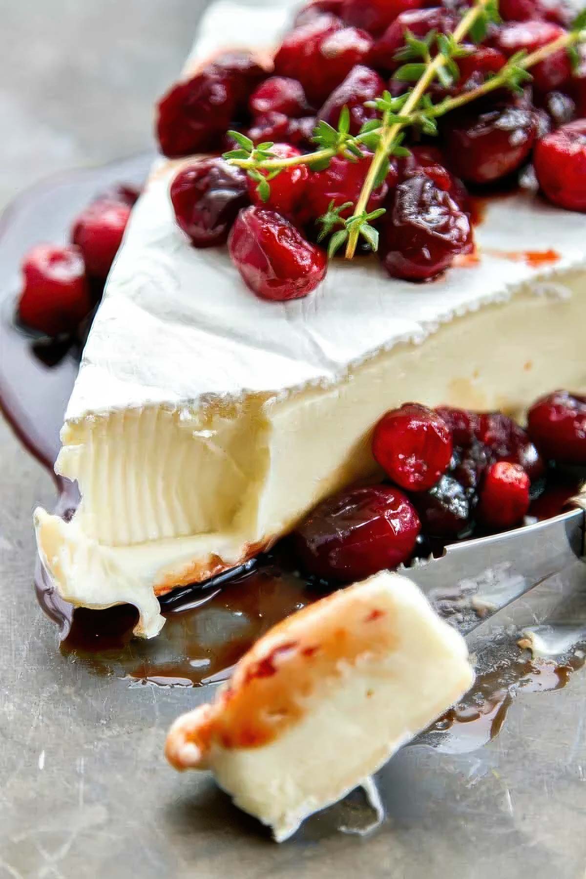a wedge of cranberry baked brie with a small amount of the brie on an appetizer knife, garnished with fresh sprigs of thyme