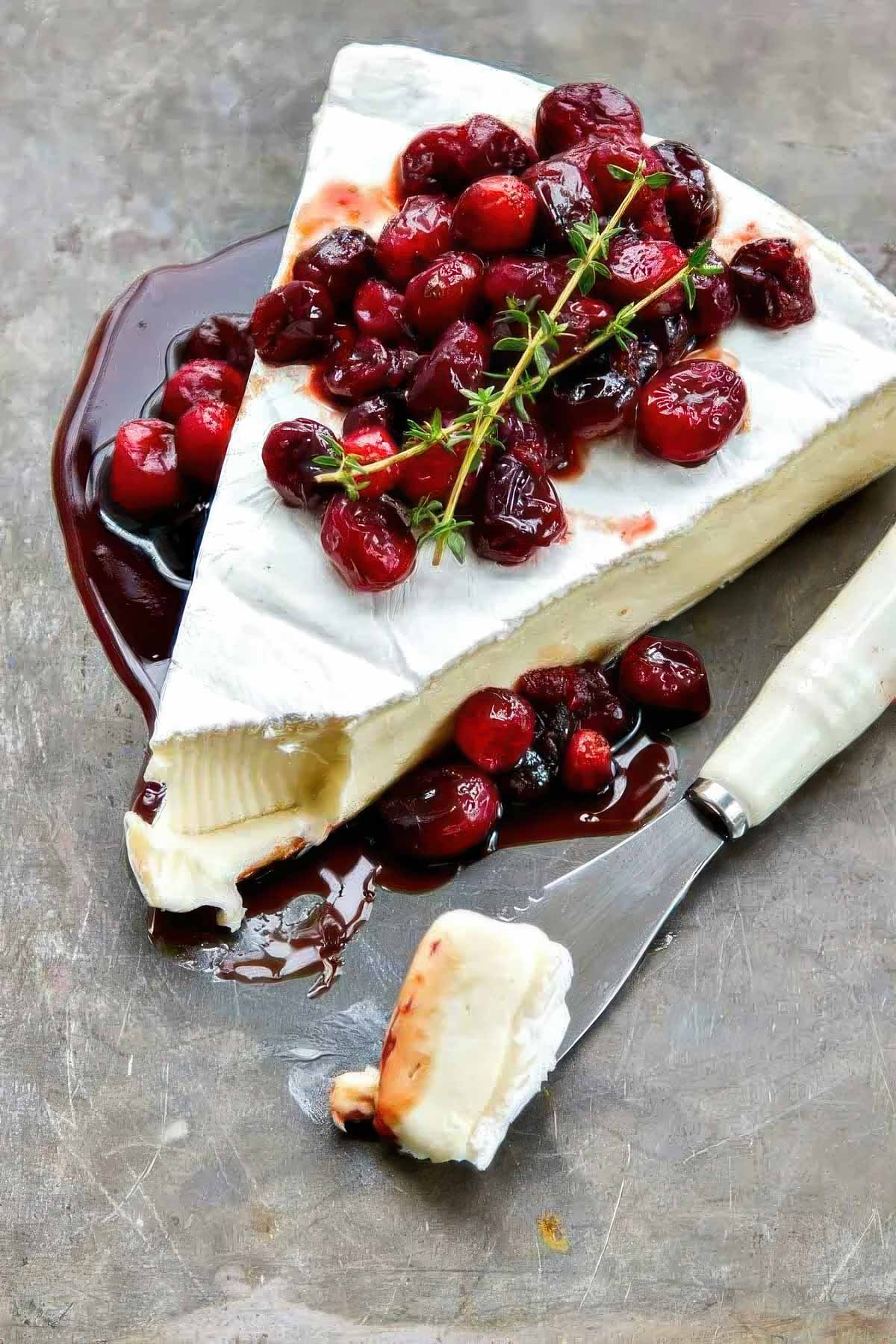 a wedge of cranberry baked brie with a small amount of the brie on an appetizer knife, garnished with fresh sprigs of thyme