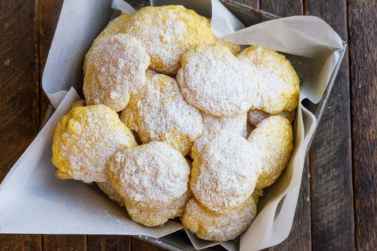 a vintage metal baking pan lined with parchment paper and filled with lemon cake mix cookies sprinkled with powdered sugar