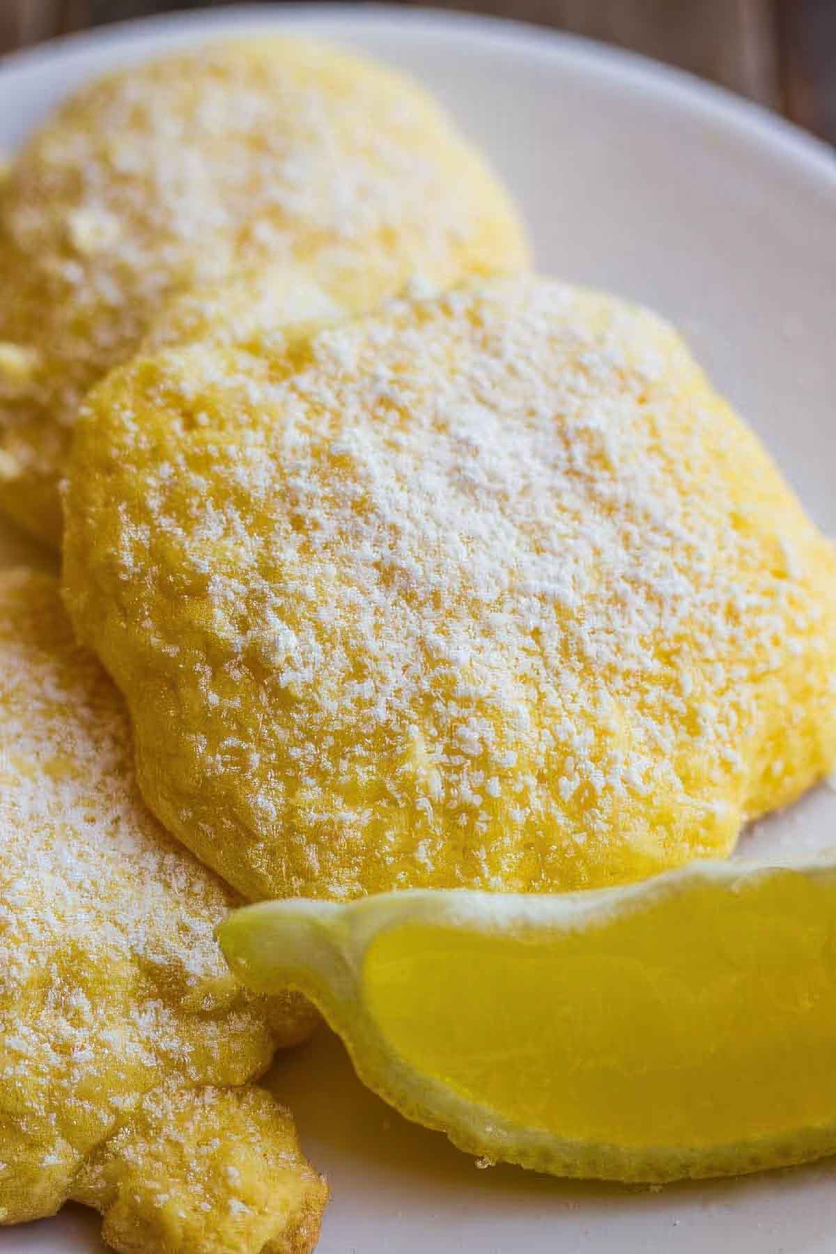 a closeup of a lemon cake mix cookie next to a fresh lemon wedge on a white plate